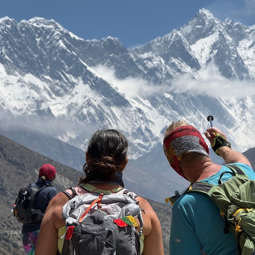 Three people with backpacks looking at snow-capped Mount Everest in Nepal.