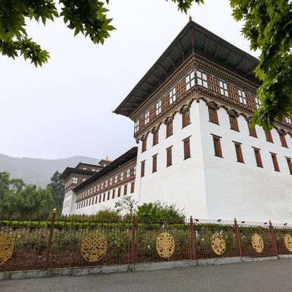 Traditional Bhutanese building with white walls and wooden accents, surrounded by greenery.
