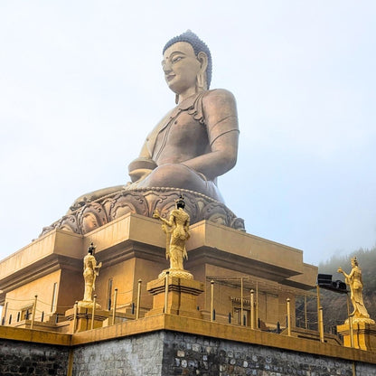 Large Buddha statue on a pedestal with golden statues in front, against a clear sky.